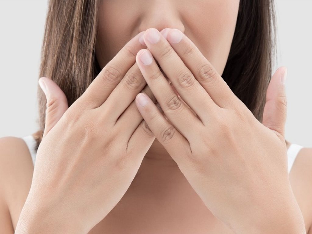 Una ragazza con le mani davanti alla bocca per colpa dell'alitosi o alito cattivo