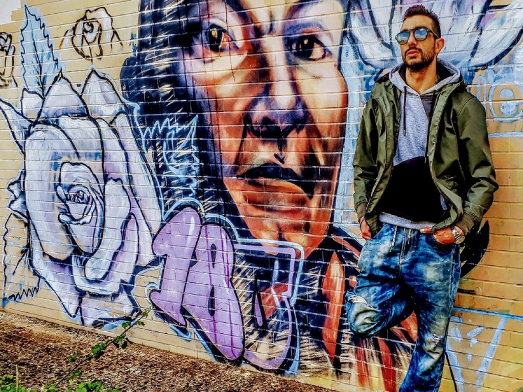 Il rapper Lo Scomodo appoggiato a un murales