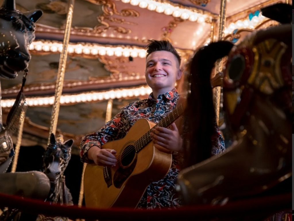 Il cantante Lorenzo Polidori con la sua chitarra su una giostra