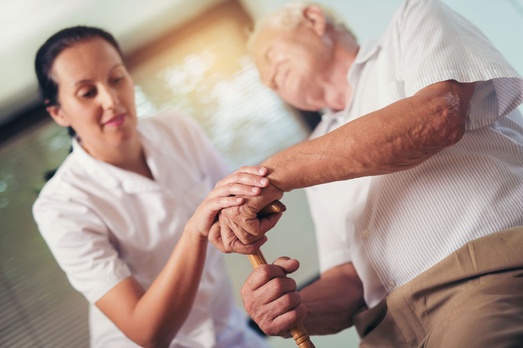 Un anziano malato di Parkinson con bastone aiutato da infermiera nel piano nazionale cronicità