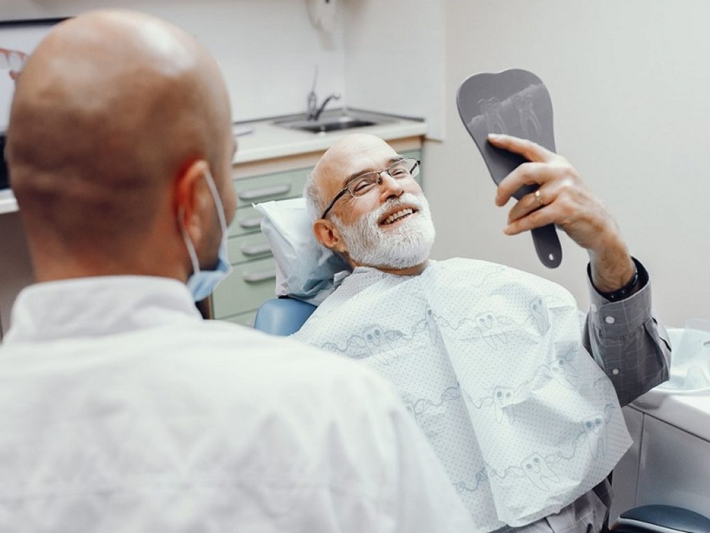 Paziente su lettino si guarda allo specchio dal dentista dopo impianto dentale